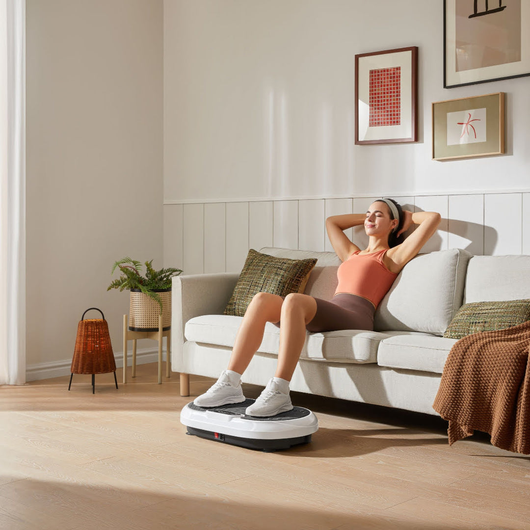 Woman sitting on couch with arms behind head and feet on vibration plate.
