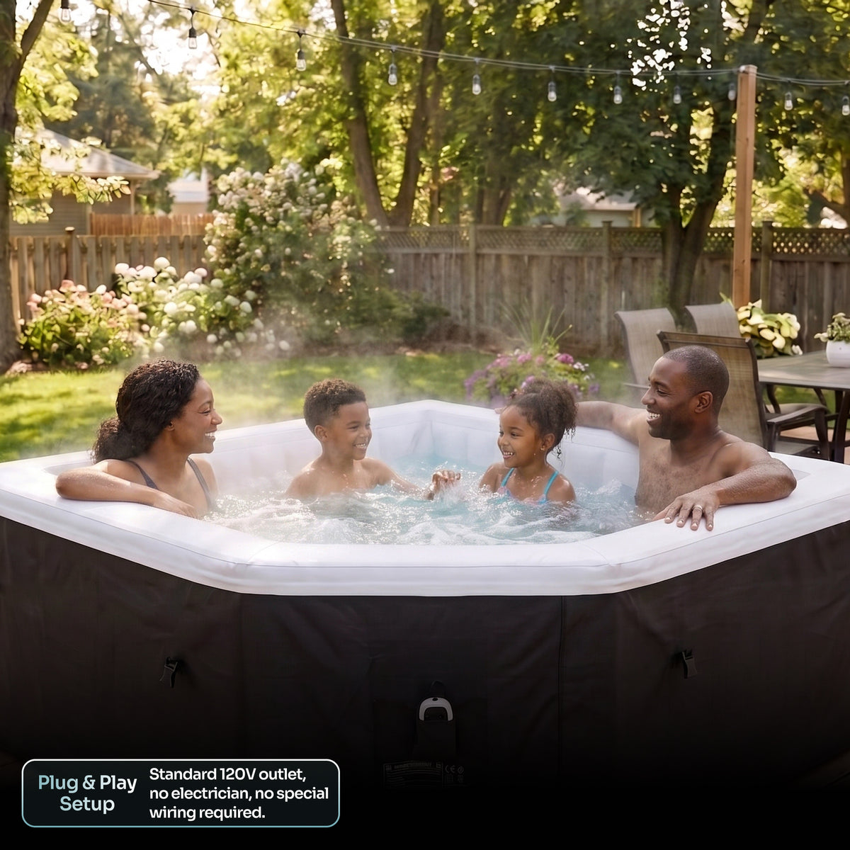 A family of four enjoys a hot spring outdoor tub in a backyard setting. The tub has a black exterior cover and a white interior, with bubbling water creating a misty atmosphere.