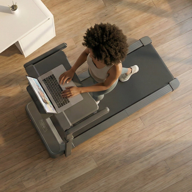 Person using a laptop on a treadmill in a modern Manhattan New York office setting with large windows.