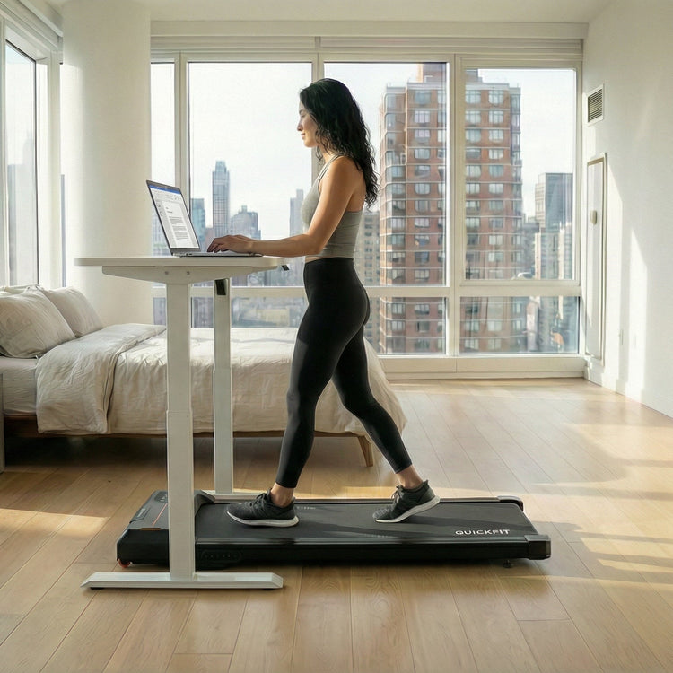 Person using a walking pad treadmill desk in a modern apartment bed room with large windows.