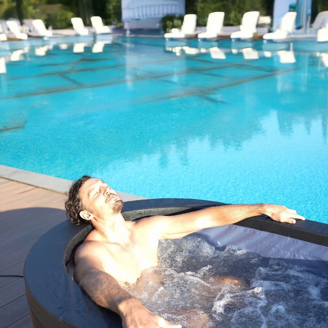 Man relaxing inside spa beside large pool.