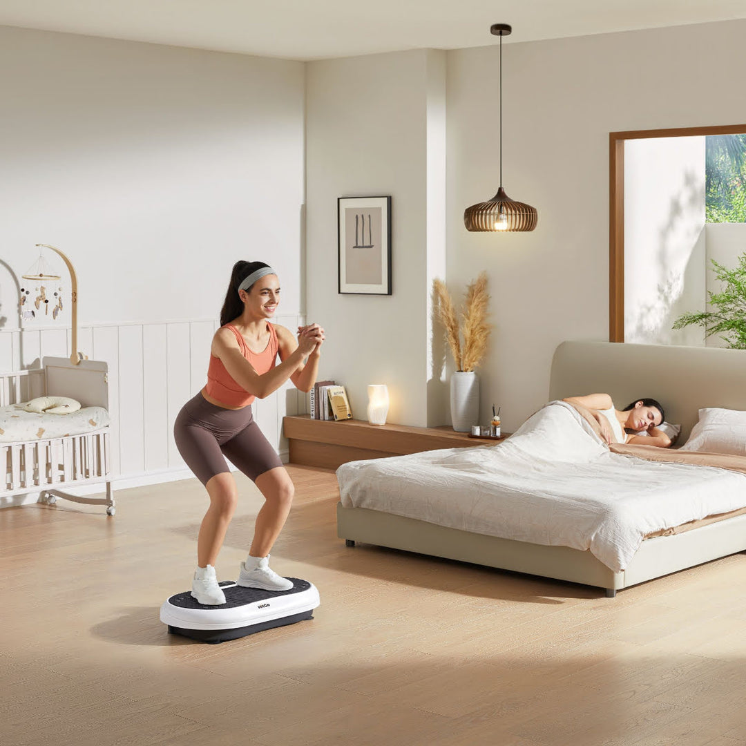 Woman exercising on vibration plate in bedroom, while someone is sleeping in bed.