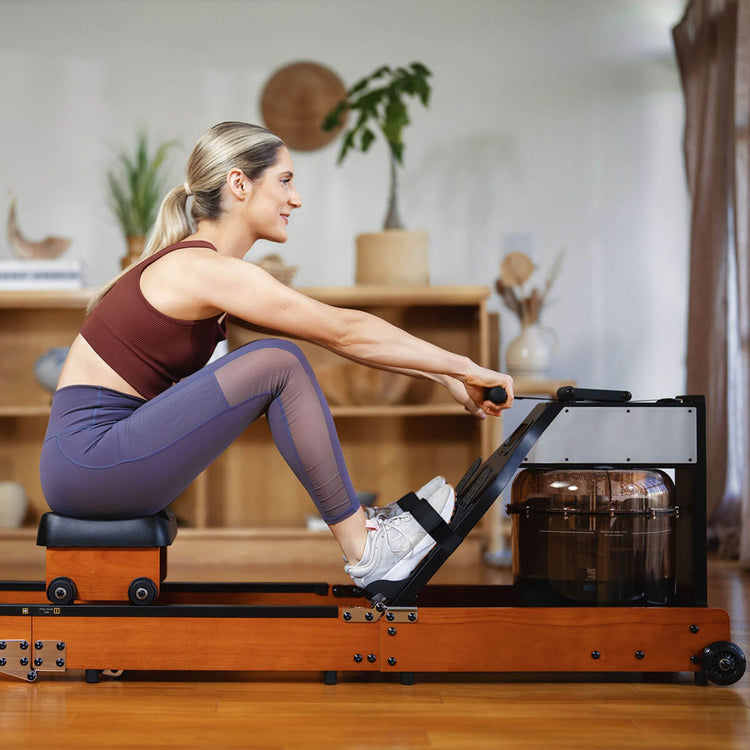 A person using a foldable water rowing machine in a home setting, with the machine showing a wooden frame and a water tank.