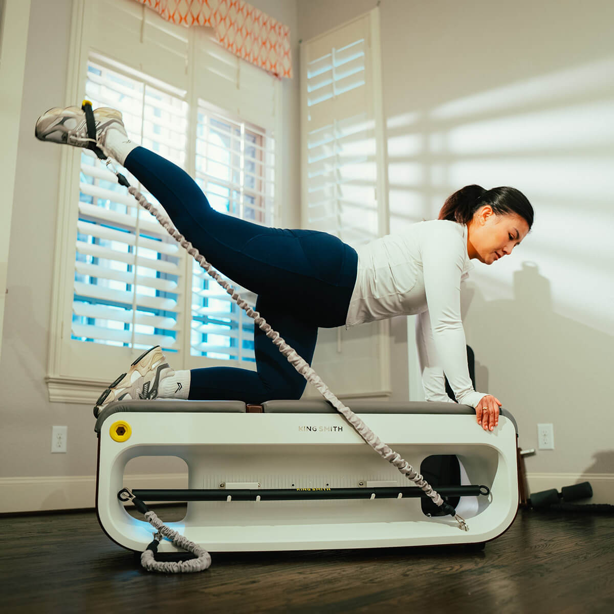 A woman working out on the workout bench using the exercise bands kicking back with her leg in the air.