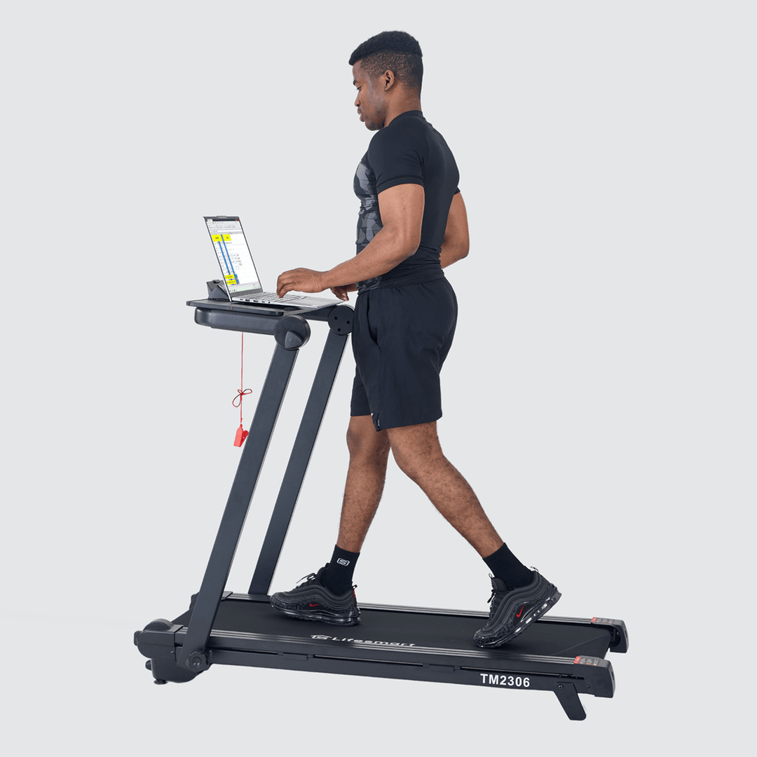 Man walking on treadmill while working on laptop laying on console desk.