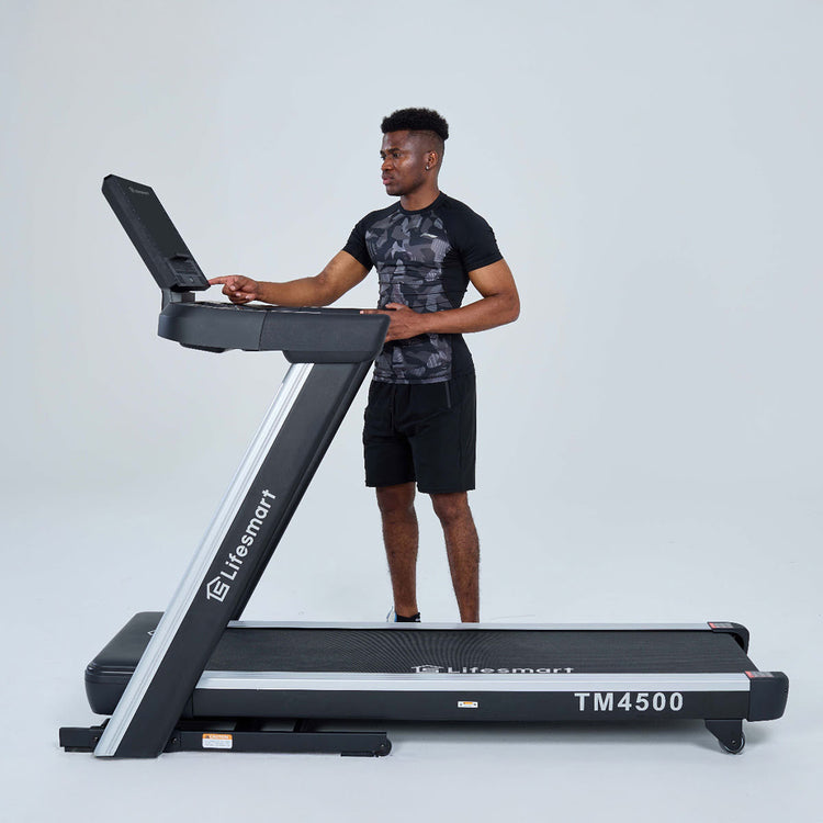 Man standing behind treadmill pressing the Power Touch button on side of console.