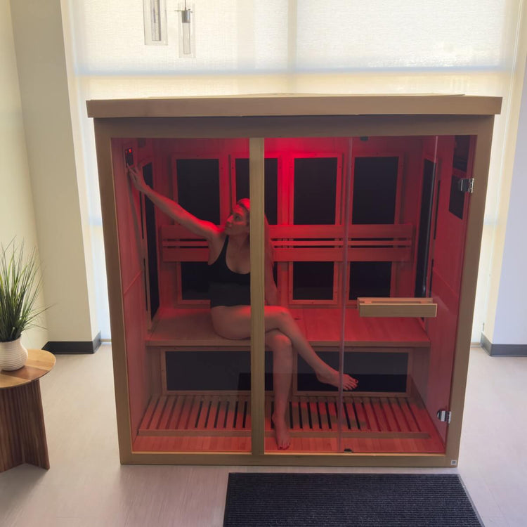 Woman sitting inside of sauna with red light inside. She is adjusting the temperature by pressing the control panel inside.