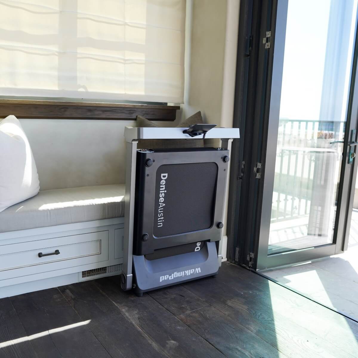 The Denise Austin 2.0 WalkingPad folded vertically against the wall in home setting.