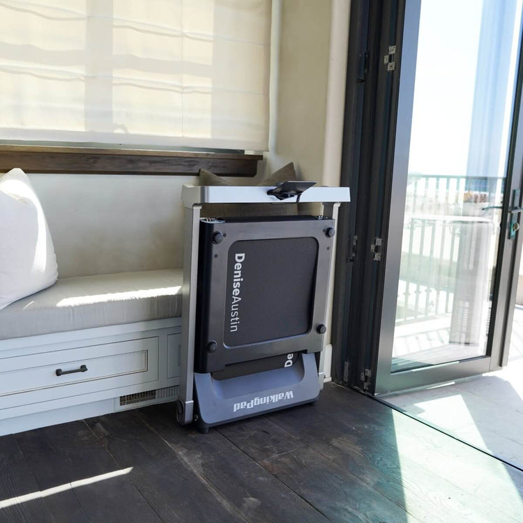 The Denise Austin 2.0 WalkingPad folded vertically against the wall in home setting.